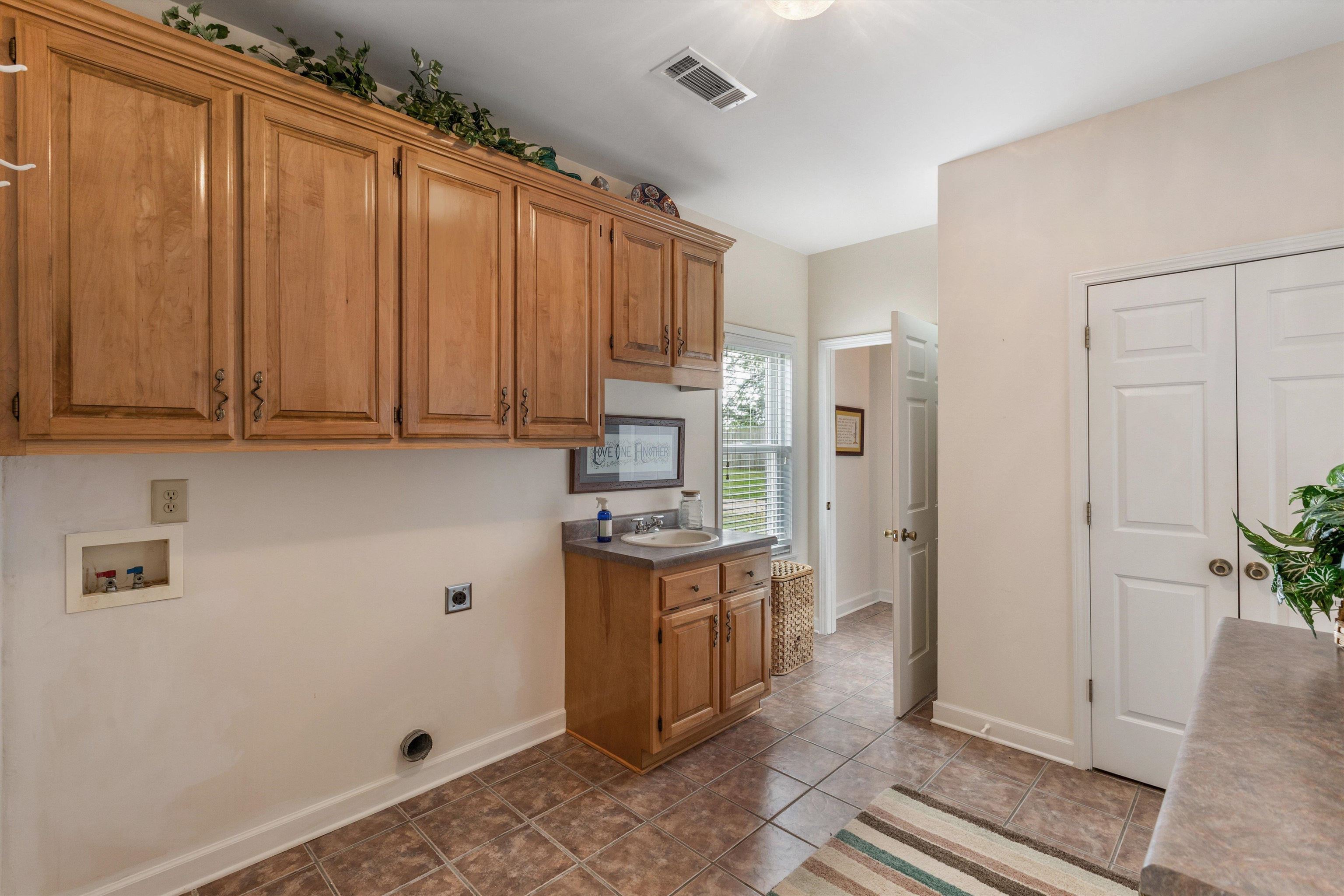 2225 Candy Lane Burlison, TN 38015 - Photo 12 of 27 Laundry area featuring extensive wood-finish cabinetry, a utility sink with a laminate countertop, tiled flooring, and a large window providing natural light