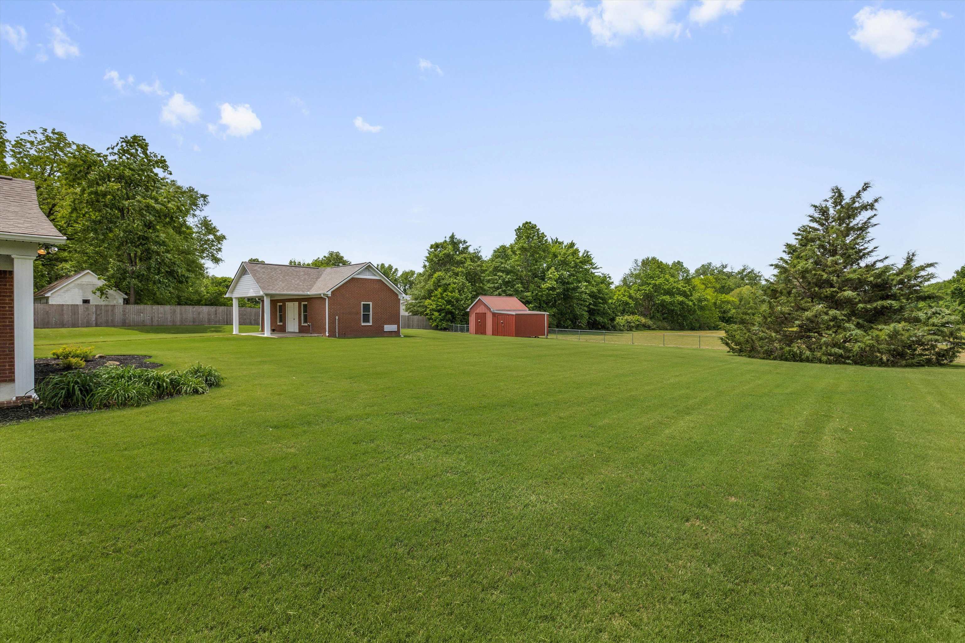 2225 Candy Lane Burlison, TN 38015 - Photo 19 of 27 Expansive green lawn featuring a red brick structure with a covered porch, a separate red storage shed, and mature trees