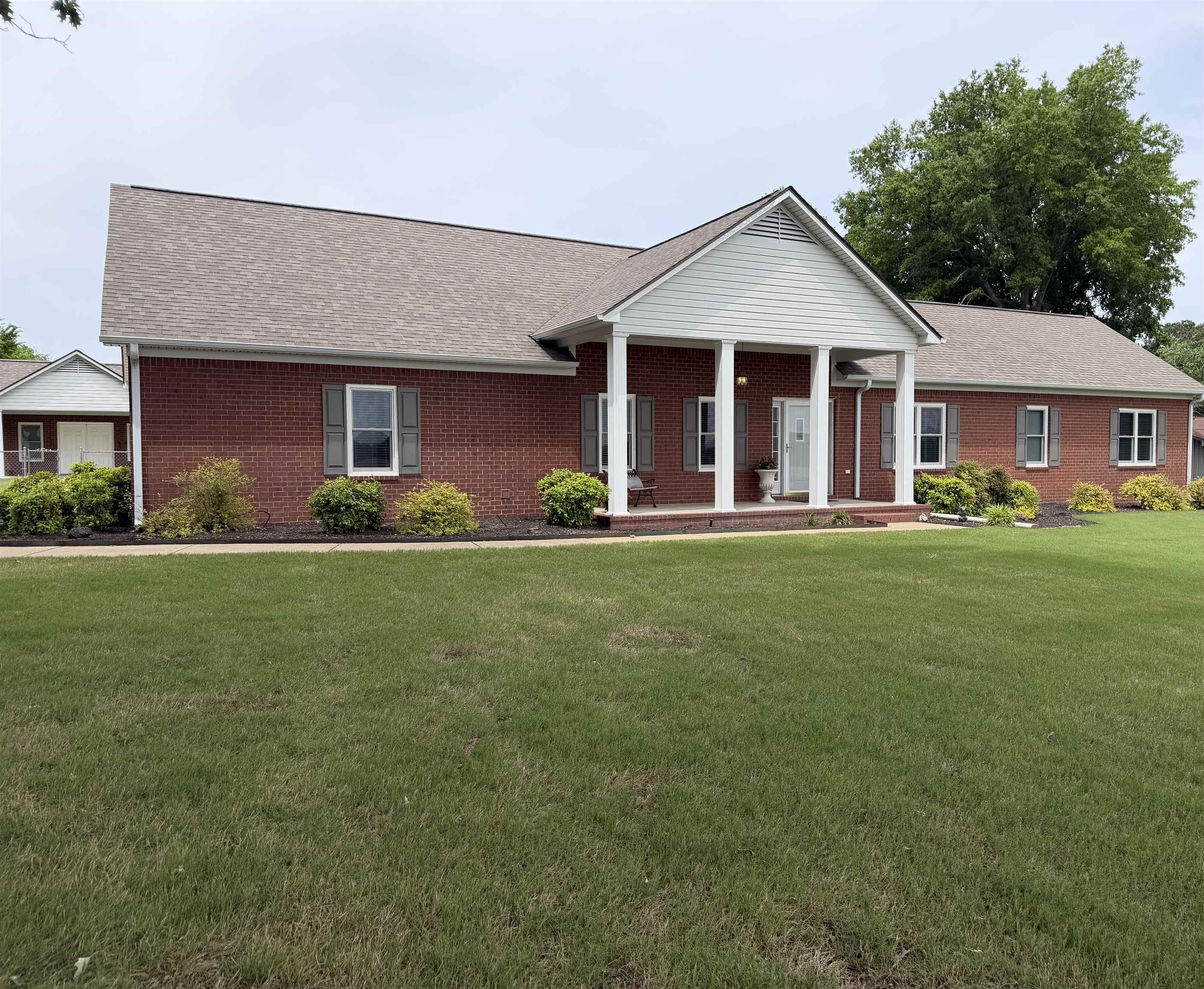 2225 Candy Lane Burlison, TN 38015 - Photo 23 of 27 Brick exterior residence featuring a covered front porch with white columns, dark shutters, and a brown shingle roof