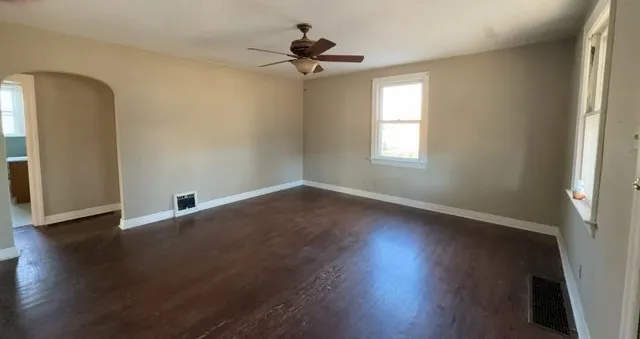 an empty room with wooden floor chandelier fan and windows