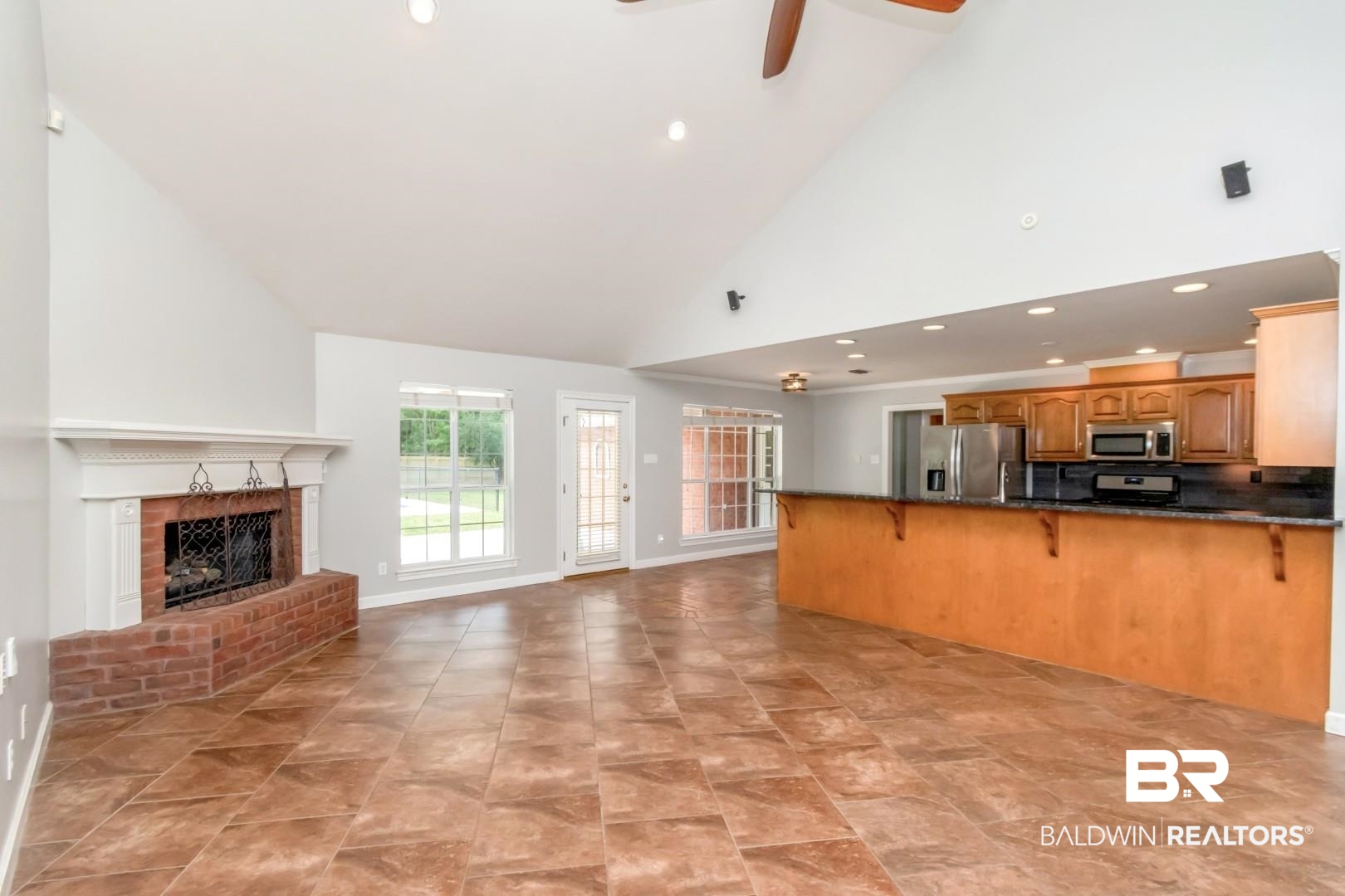 10691 Hunters Ridge Drive Mobile, AL 36695 - Photo 8 of 37 Vaulted living space featuring a brick fireplace with a white mantel, tiled flooring, and an open-concept kitchen with a breakfast bar, wood cabinetry, and stainless steel appliances