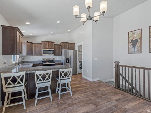 573 South Maxwell Drive Grantsville, UT 84029 - Photo 9 of 25 Kitchen with a peninsula, dark wood finish cabinetry, stainless steel appliances, a kitchen breakfast bar, and dark wood-style flooring