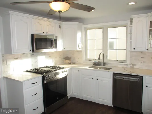 a kitchen with stainless steel appliances granite countertop white cabinets a sink and a window