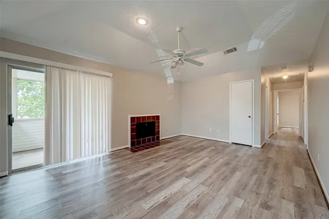 an empty room with wooden floor fan and windows