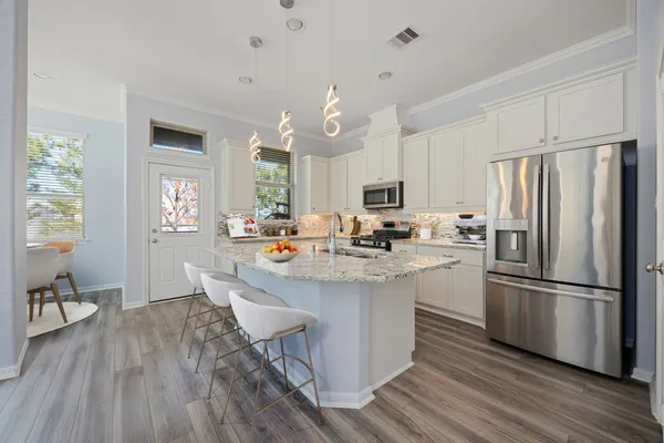 a kitchen with stainless steel appliances a dining table chairs refrigerator sink and cabinets