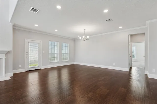 an empty room with wooden floor chandelier and windows
