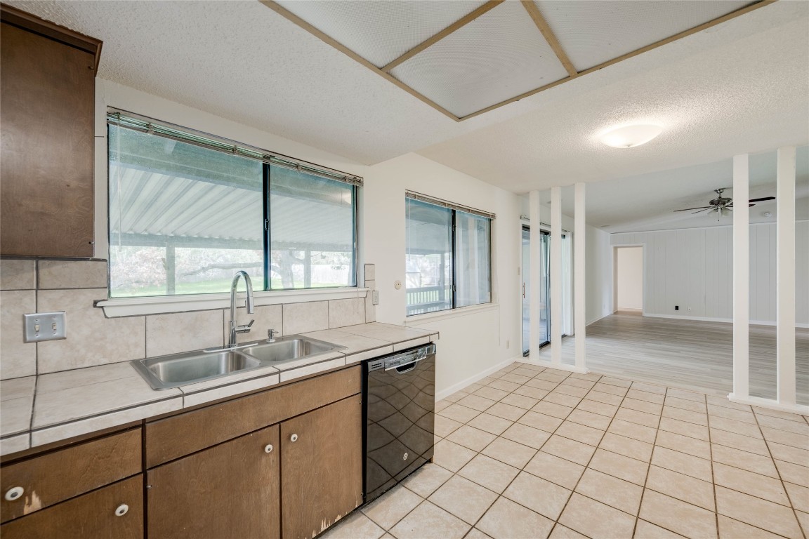 1402 Meadgreen Circle Austin, TX 78758 - Photo 16 of 35 Kitchen with tile countertops, dishwasher, a textured ceiling, light tile patterned flooring, and brown cabinets