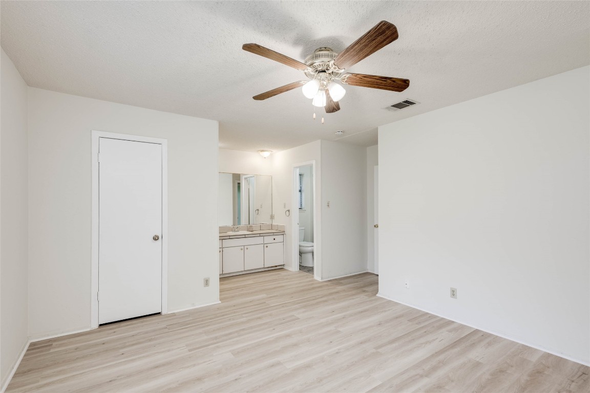 1402 Meadgreen Circle Austin, TX 78758 - Photo 21 of 35 Unfurnished bedroom featuring light wood-style floors, ceiling fan, connected bathroom, and a textured ceiling