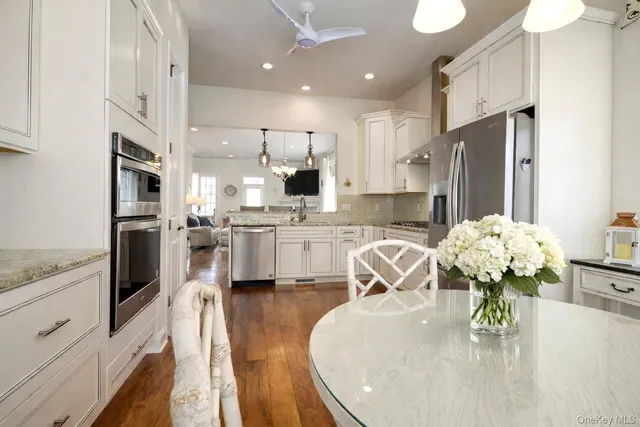 a kitchen with stainless steel appliances granite countertop a refrigerator a sink dishwasher a stove a dining table and chairs with wooden floor