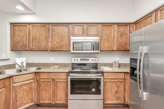 a kitchen with stainless steel appliances granite countertop a refrigerator stove top oven and sink with cabinets