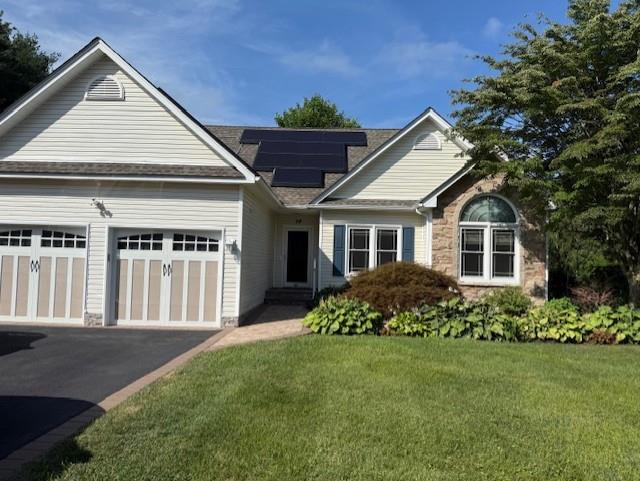 View of front of house featuring roof mounted solar panels, a front yard, driveway, a garage, and stone siding