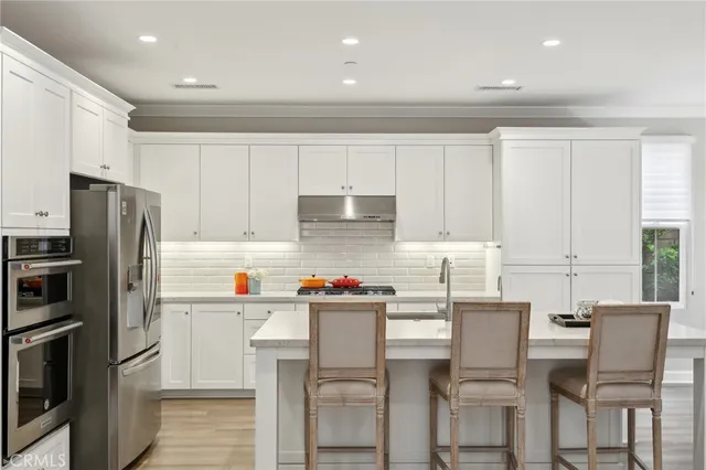 a kitchen with stainless steel appliances a dining table chairs refrigerator and sink
