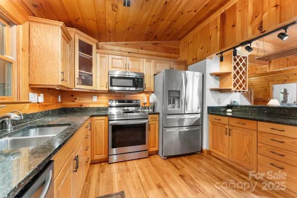 a kitchen with stainless steel appliances granite countertop a refrigerator a sink dishwasher a stove and a microwave oven with wooden floor