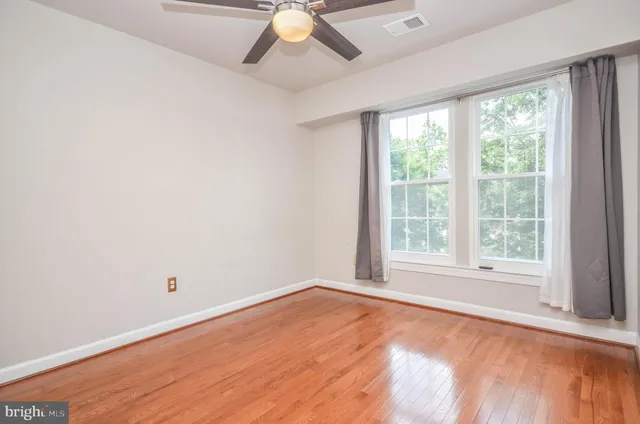 an empty room with wooden floor fan and windows