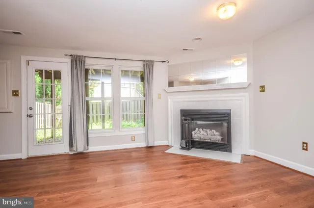 a view of an empty room with wooden floor fireplace and a window