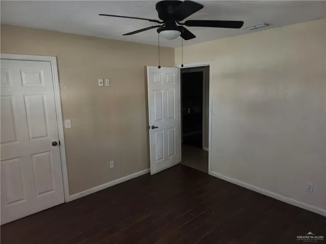 an empty room with wooden floor a ceiling fan and stainless steel appliances