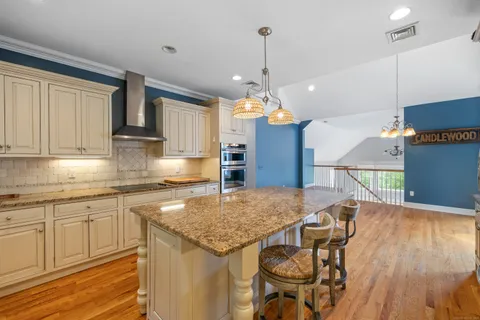 a kitchen with stainless steel appliances granite countertop a kitchen island a stove a sink a dining table and chairs with wooden floor