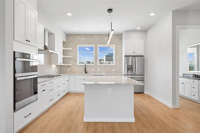 a kitchen with stainless steel appliances granite countertop a refrigerator a stove and white cabinets with wooden floors