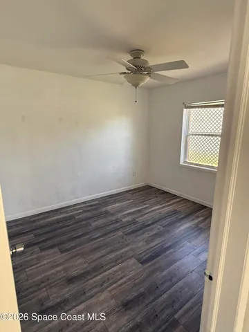 an empty room with wooden floor fan and windows