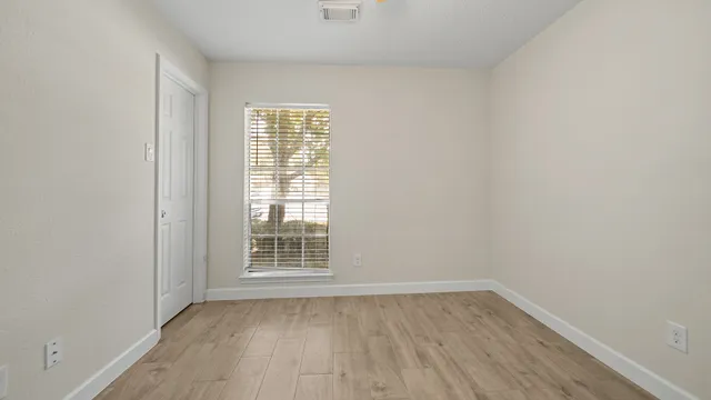 a view of an empty room with wooden floor and a window