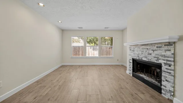 an empty room with wooden floor fireplace and windows