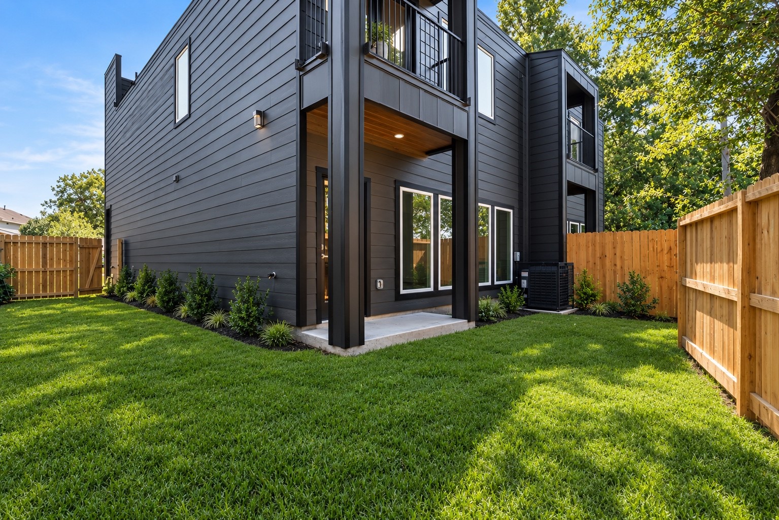 5629 Malmedy Road Houston, TX 77033 - Photo 8 of 24 Sleek modern home with striking black exterior, featuring a private, fenced backyard with lush green lawn and a covered patio area perfect for outdoor relaxation.
*landscaping is AI generated*