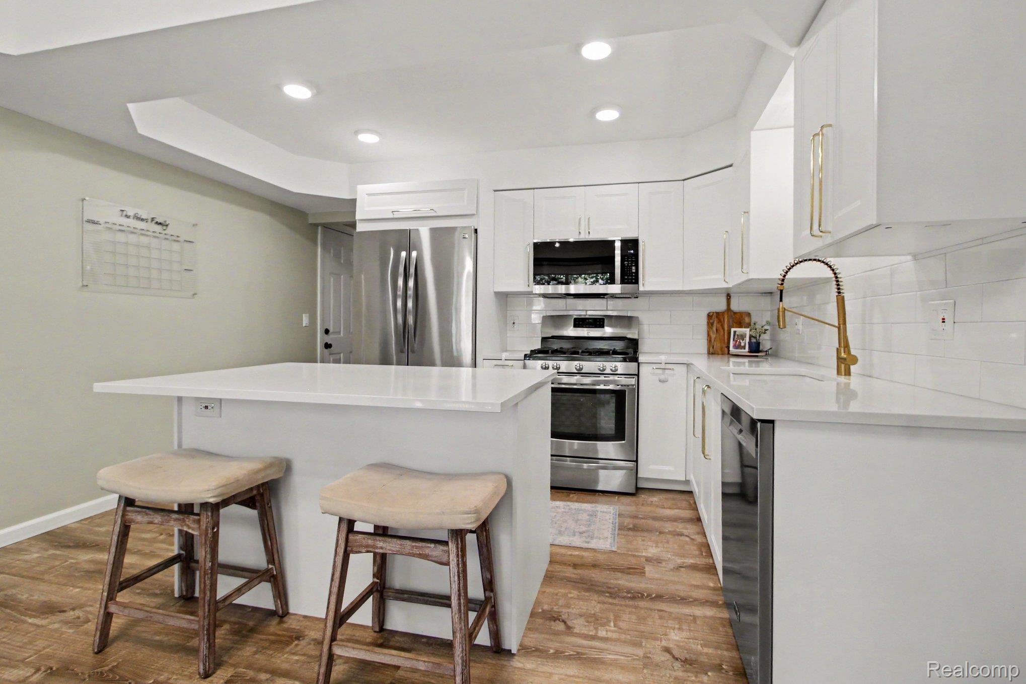 7235 Iron Gate Road Canton, MI 48187 - Photo 8 of 27 Modern kitchen featuring white cabinetry, stainless steel appliances, a white subway tile backsplash, light-toned countertops, and wood-finish flooring