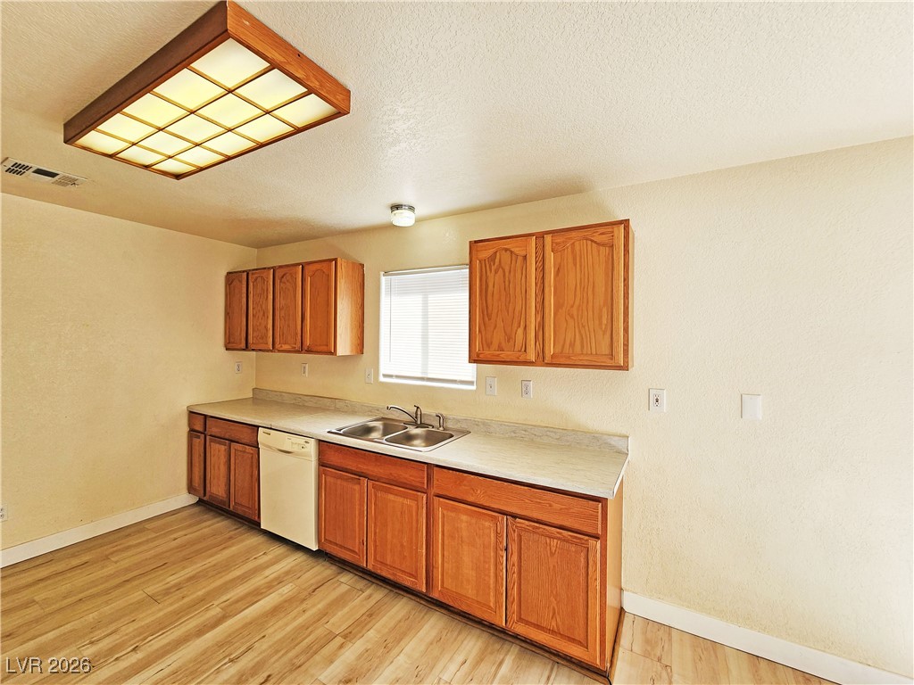1081 Marne Court, Unit C Pahrump, NV 89048 - Photo 8 of 22 Kitchen featuring light countertops, brown cabinetry, dishwasher, a textured ceiling, and light wood-type flooring