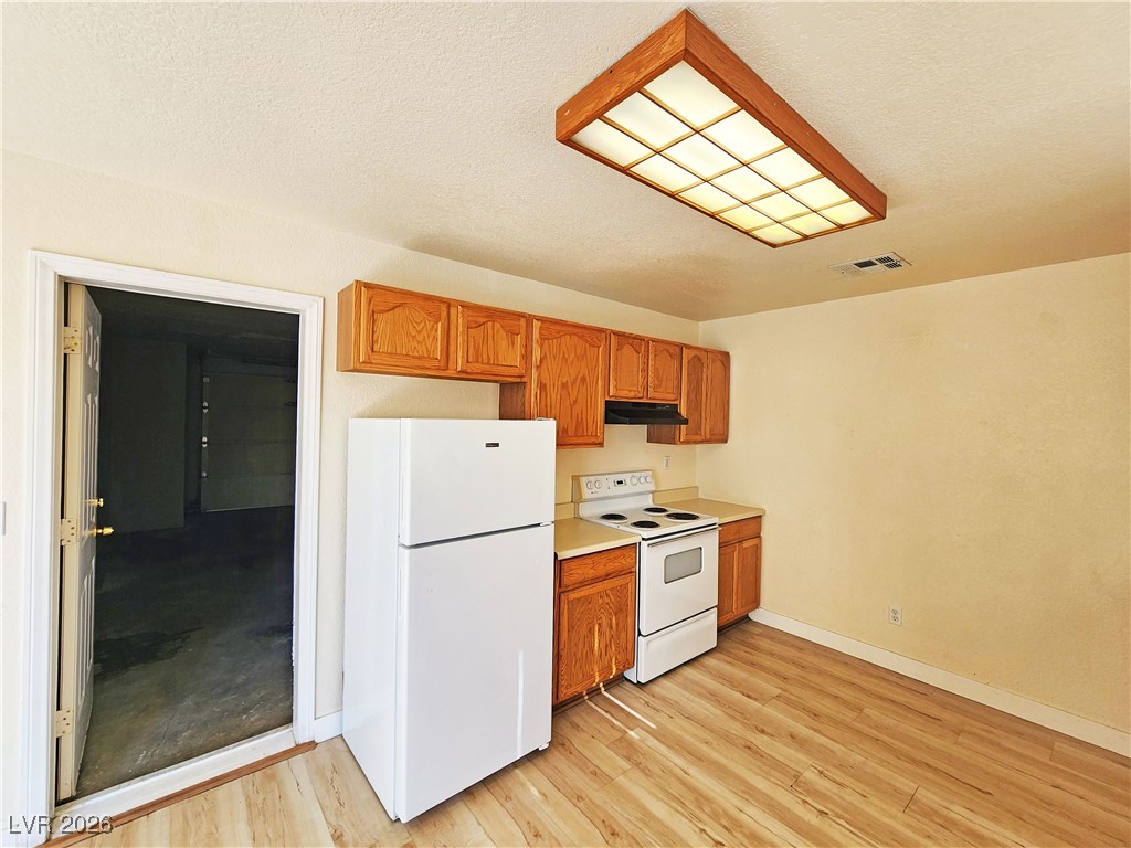 1081 Marne Court, Unit C Pahrump, NV 89048 - Photo 9 of 22 Kitchen featuring white appliances, light countertops, brown cabinetry, light wood-type flooring, and a textured ceiling