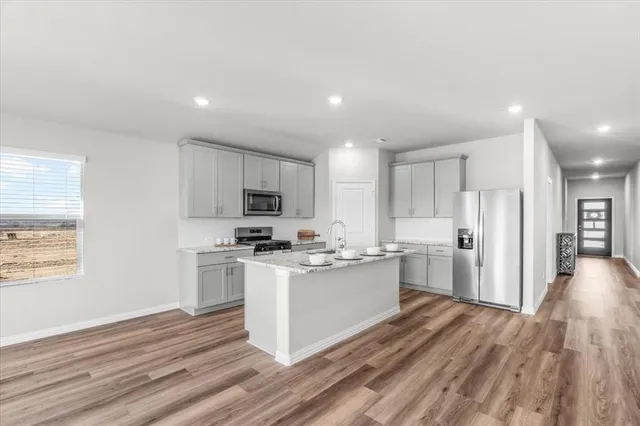 a kitchen with stainless steel appliances a stove top oven a refrigerator a sink and dishwasher with wooden floor