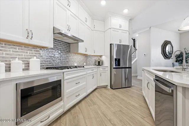 a kitchen with granite countertop a refrigerator oven a sink dishwasher and white cabinets with wooden floor