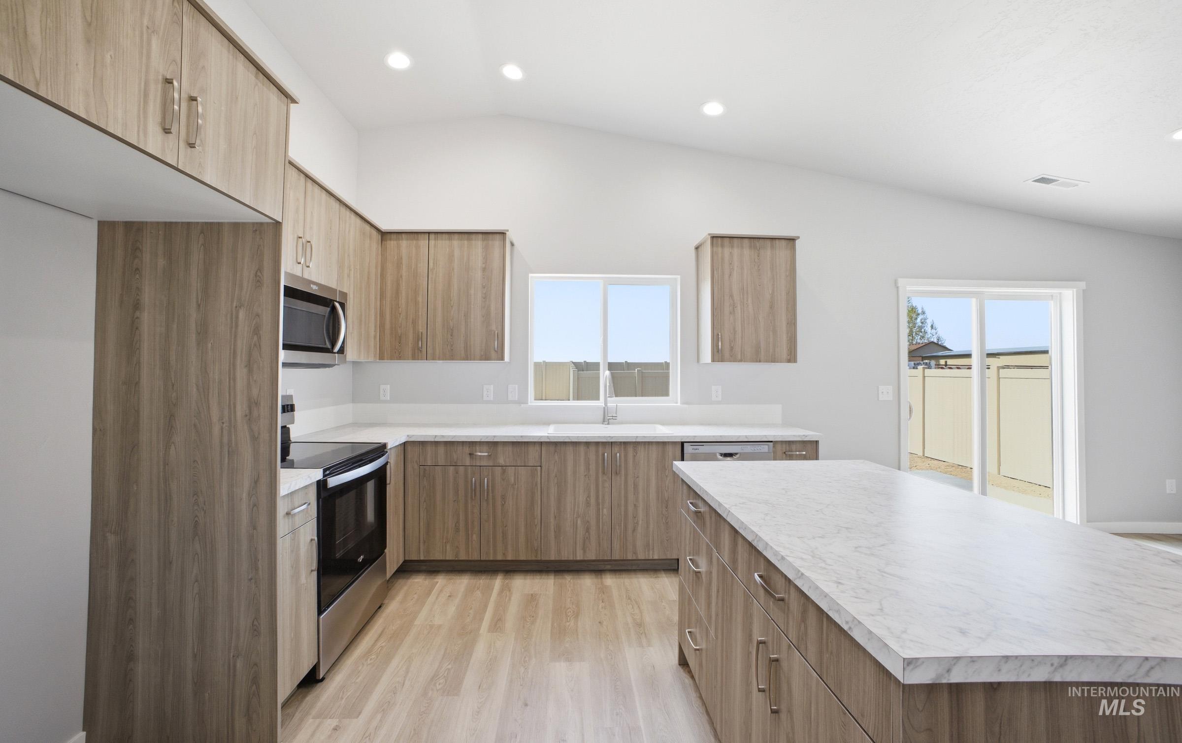 14106 Winding Street Caldwell, ID 83607 - Photo 5 of 18 Vaulted ceiling kitchen featuring wood-finish cabinetry, stainless steel appliances, and light-toned countertops