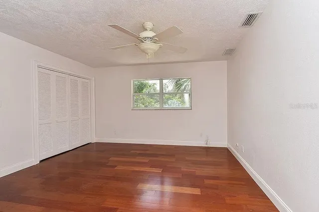 an empty room with wooden floor fan and windows