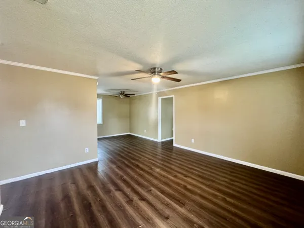 a view of an empty room with wooden floor and a ceiling fan