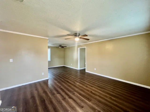 a view of an empty room with wooden floor and a ceiling fan