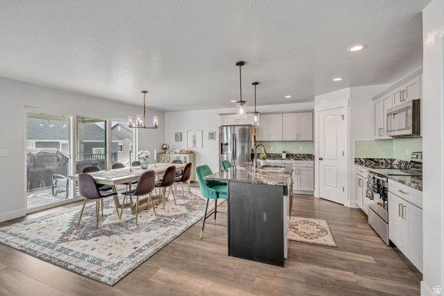 1577 Quailhill Road Saratoga Springs, UT 84045 - Photo 11 of 46 Kitchen featuring stainless steel appliances, dark stone counters, a breakfast bar, a kitchen island with sink, and suspended lighting