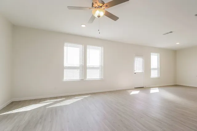 an empty room with wooden floor chandelier fan and windows