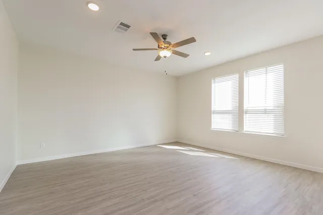 an empty room with wooden floor fan and windows