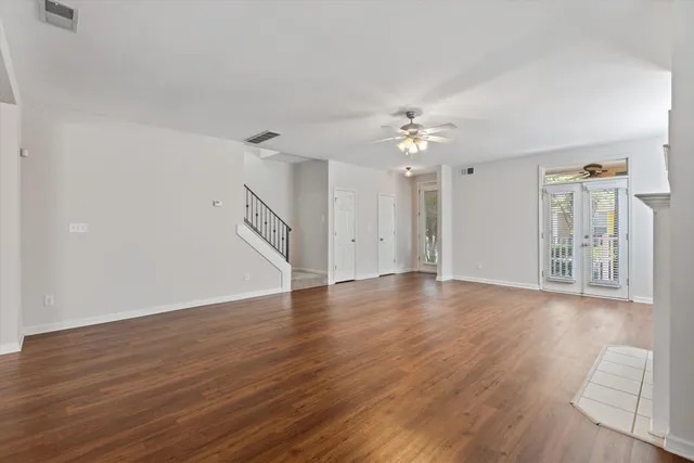 a view of an empty room with wooden floor and a ceiling fan