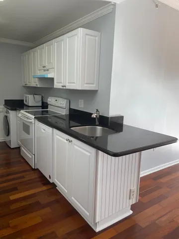 a kitchen with granite countertop a stove a sink and white cabinets