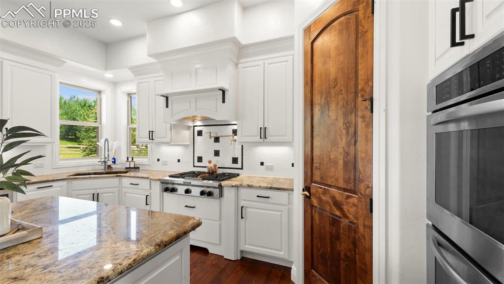 13625 Random Ridge View Colorado Springs, CO 80921 - Photo 11 of 50 Kitchen with white cabinets, light stone countertops, decorative backsplash, dark wood finished floors, and recessed lighting