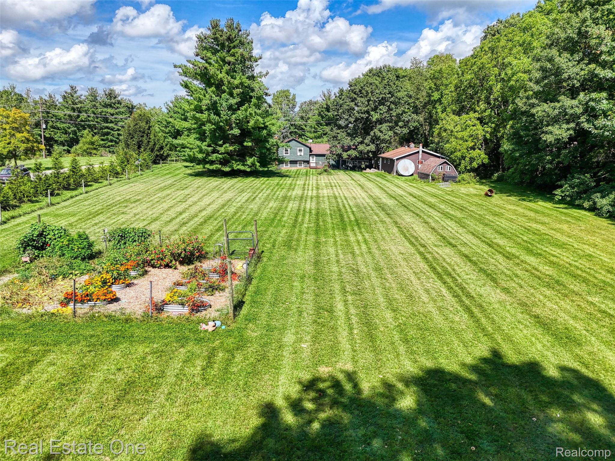 5130 Iosco Road Webberville, MI 48892 - Photo 12 of 39 Expansive green lawn with established garden beds, mature trees, a detached outbuilding, and a residential structure