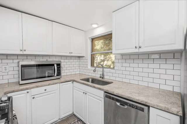 a kitchen with granite countertop white cabinets stainless steel appliances a sink and a window