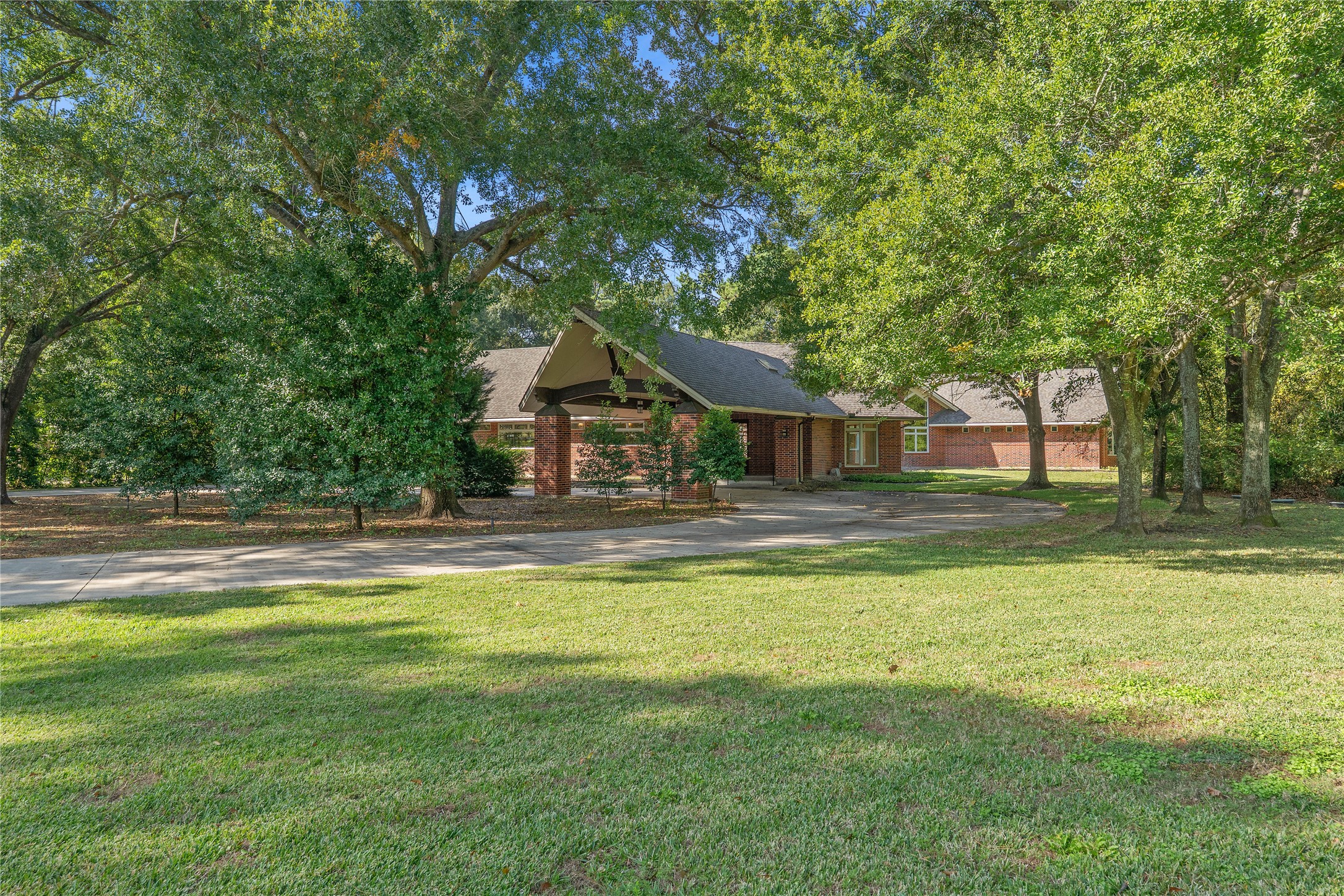 16621 Hereford Road Tomball, TX 77377 - Photo 3 of 46 Welcome to 16621 Hereford, a brick home surrounded by lush greenery and mature trees, featuring a long driveway and a welcoming entrance. The spacious front yard offers a serene, private setting.