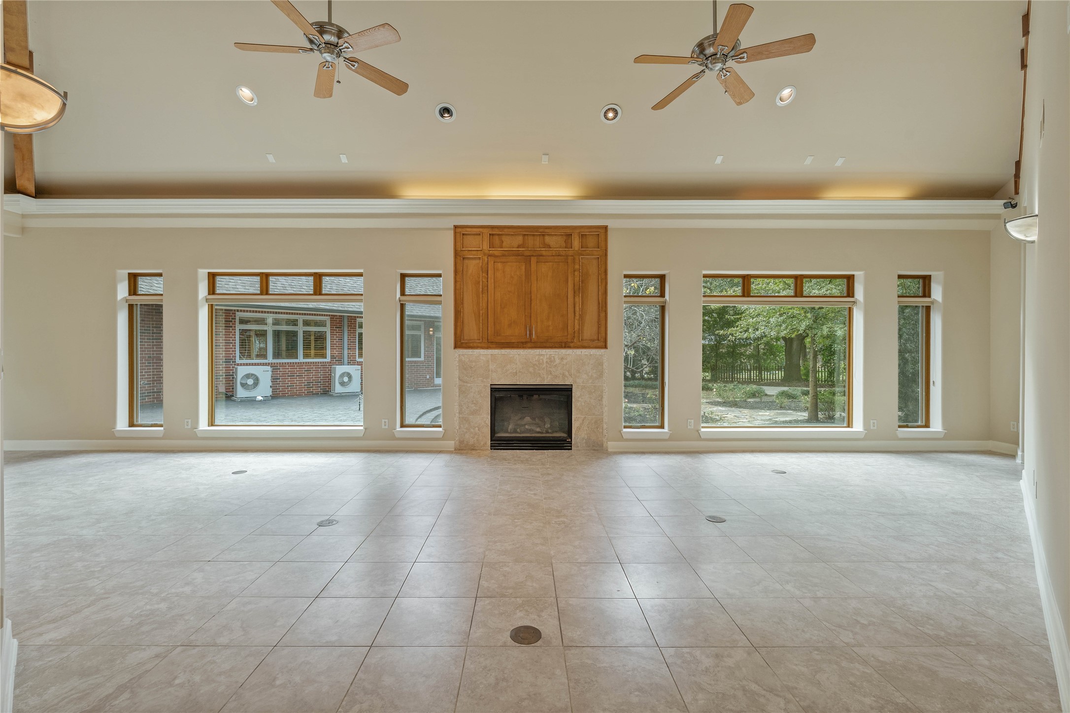 16621 Hereford Road Tomball, TX 77377 - Photo 10 of 46 Spacious living room with high ceilings, featuring a central fireplace and large windows offering plenty of natural light and views of the backyard. The tiled floor and ceiling fans add to the room's elegance and comfort.