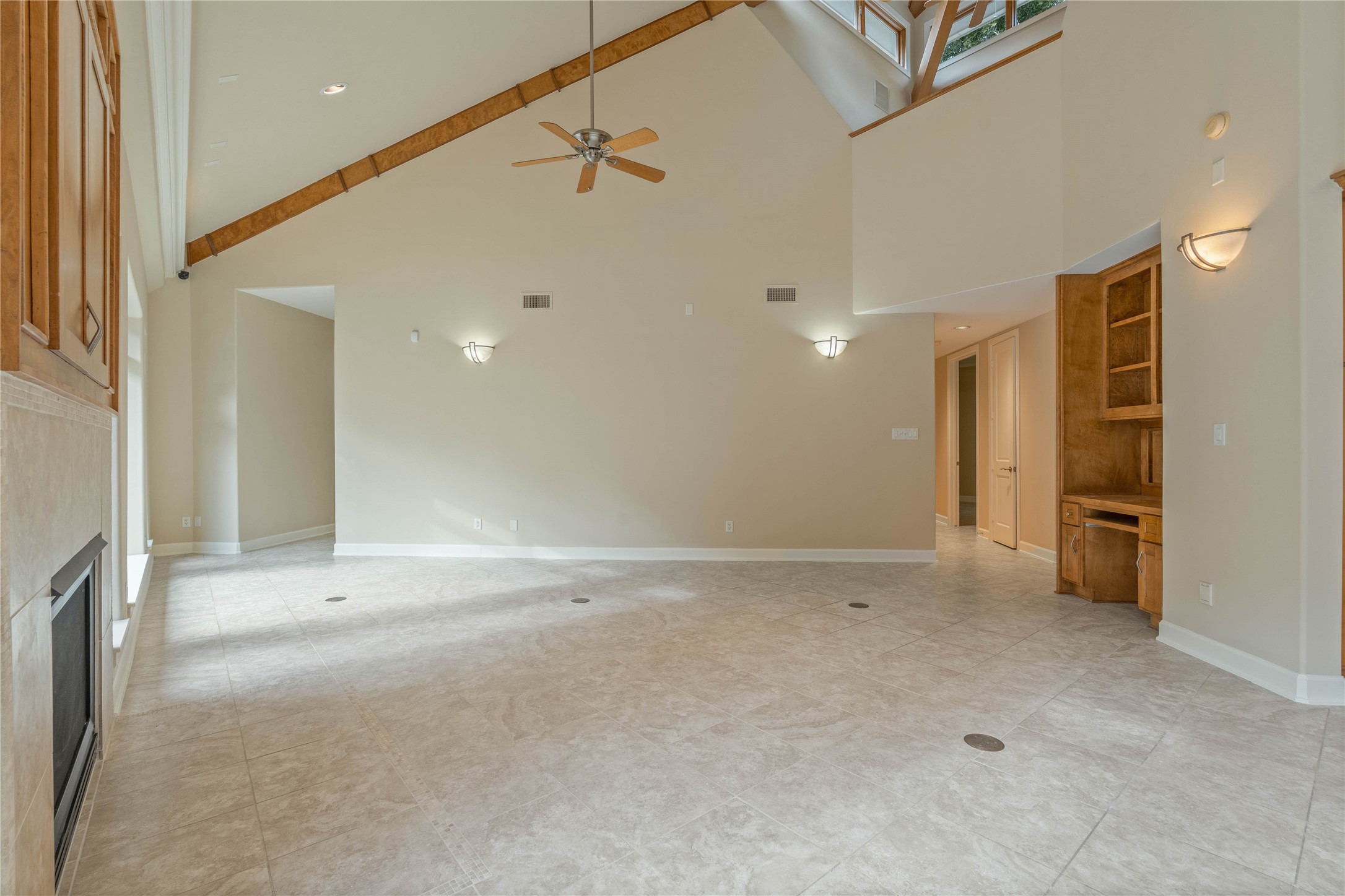 16621 Hereford Road Tomball, TX 77377 - Photo 10 of 46 This spacious living area features high vaulted ceilings with exposed wooden beams, a ceiling fan, and a cozy fireplace. The room is well-lit with natural light from large windows, and it includes a built-in wooden desk and shelving area.