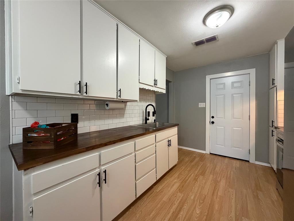 508 Batterson Street Cleburne, TX 76031 - Photo 14 of 28 Kitchen featuring white cabinetry with matte black hardware, wood-finish countertops, subway tile backsplash, and light wood-look flooring