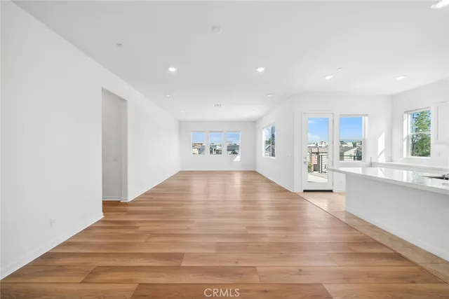 a view of an empty room and kitchen with wooden floor