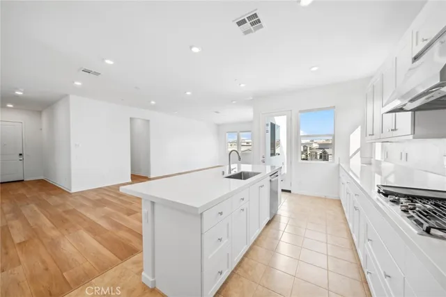 a large white kitchen with stainless steel appliances a stove a chimney a sink and cabinets