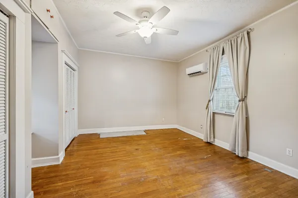 a view of an empty room with wooden floor and a ceiling fan